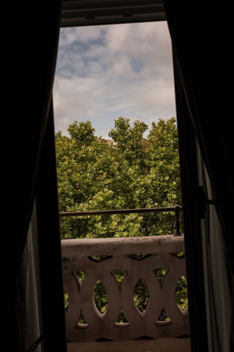 An open window onto the balcony balustrade, plane trees beyond.