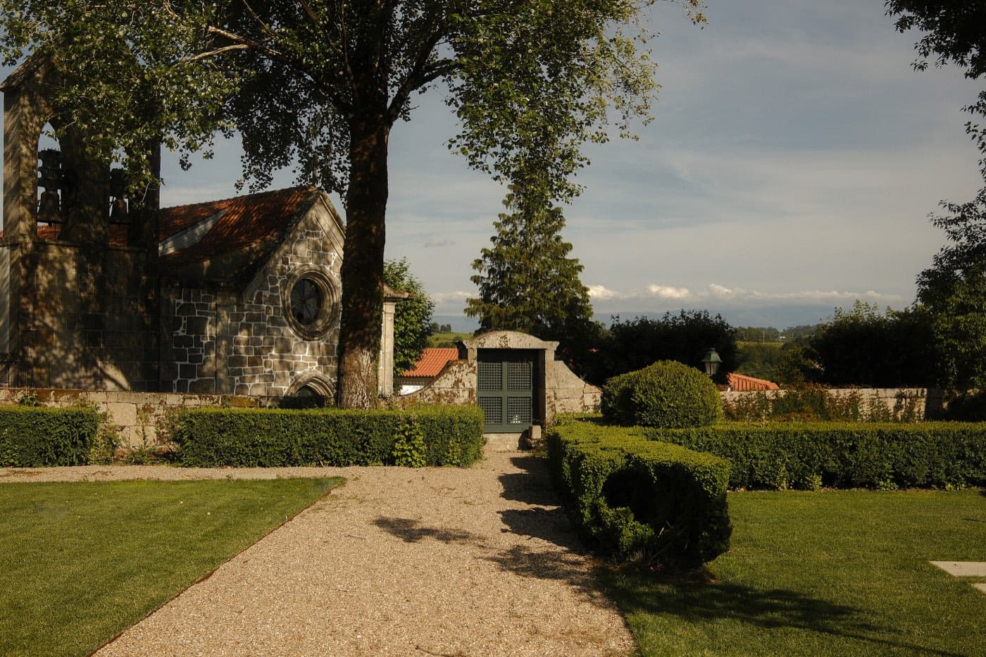 A gravel path between clipped hedges, the house to one side and open country beyond.