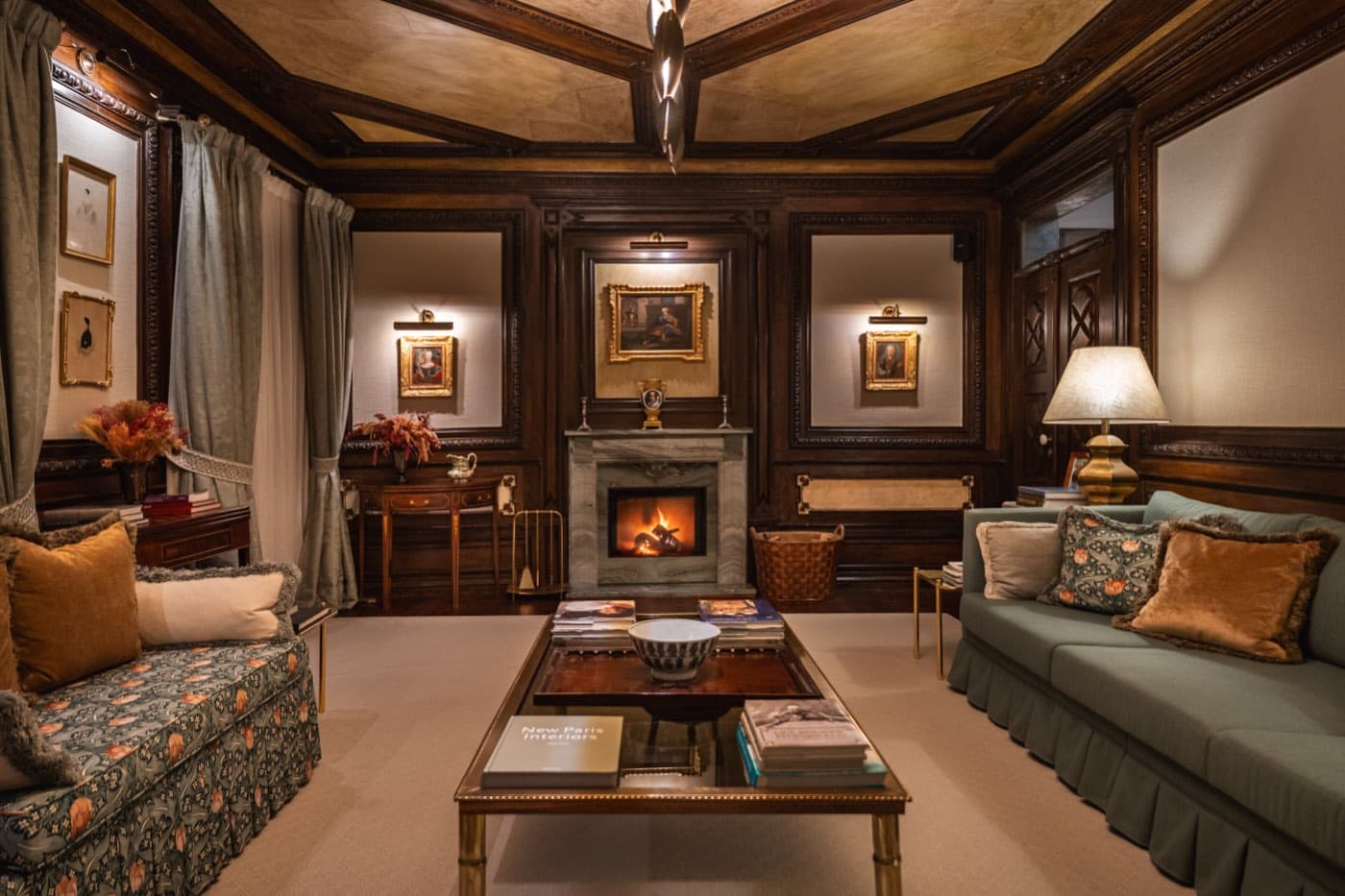 A panelled sitting room with the fire lit, sofas drawn up around a low table.