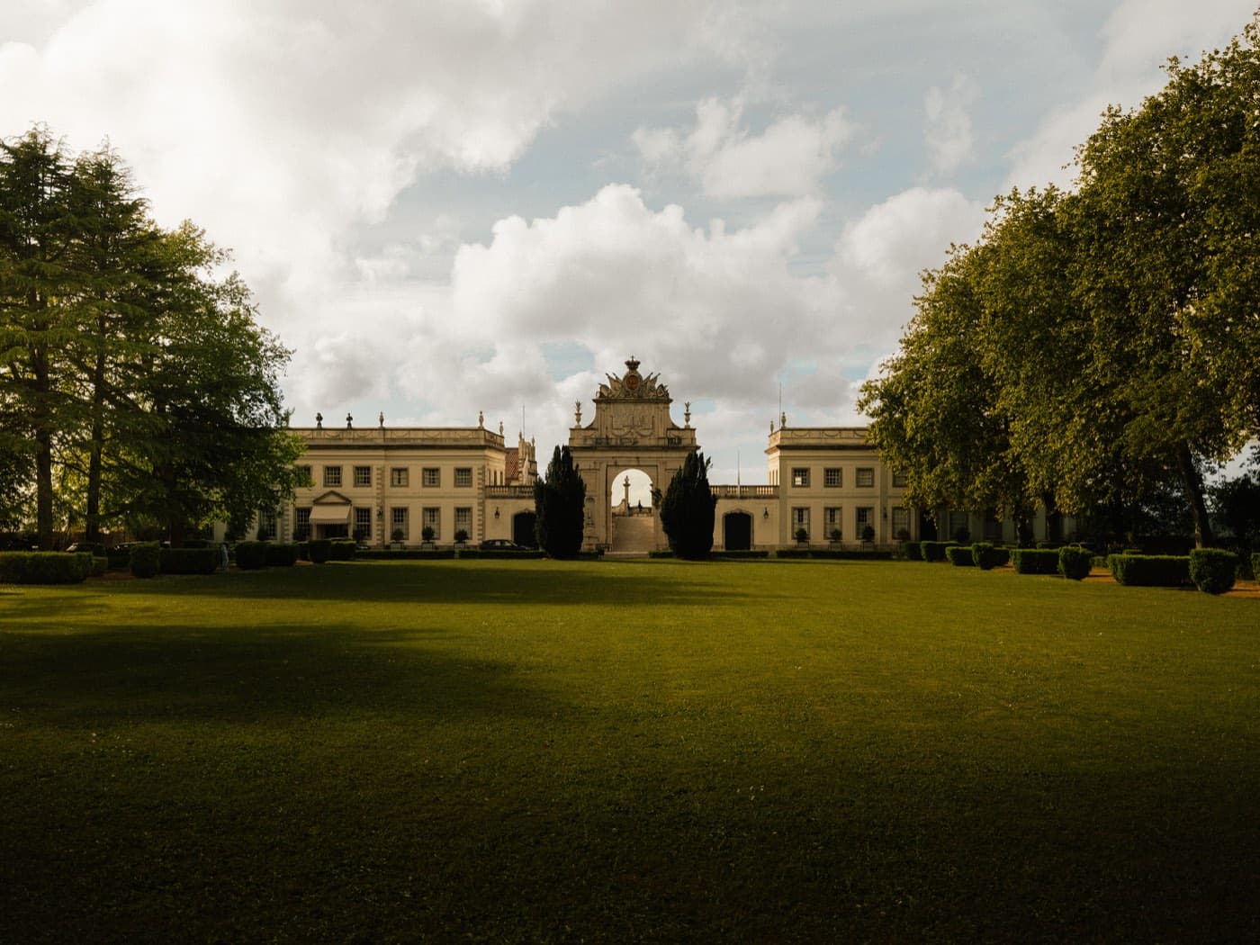 The palace across its lawn, the central arch standing between the two wings.