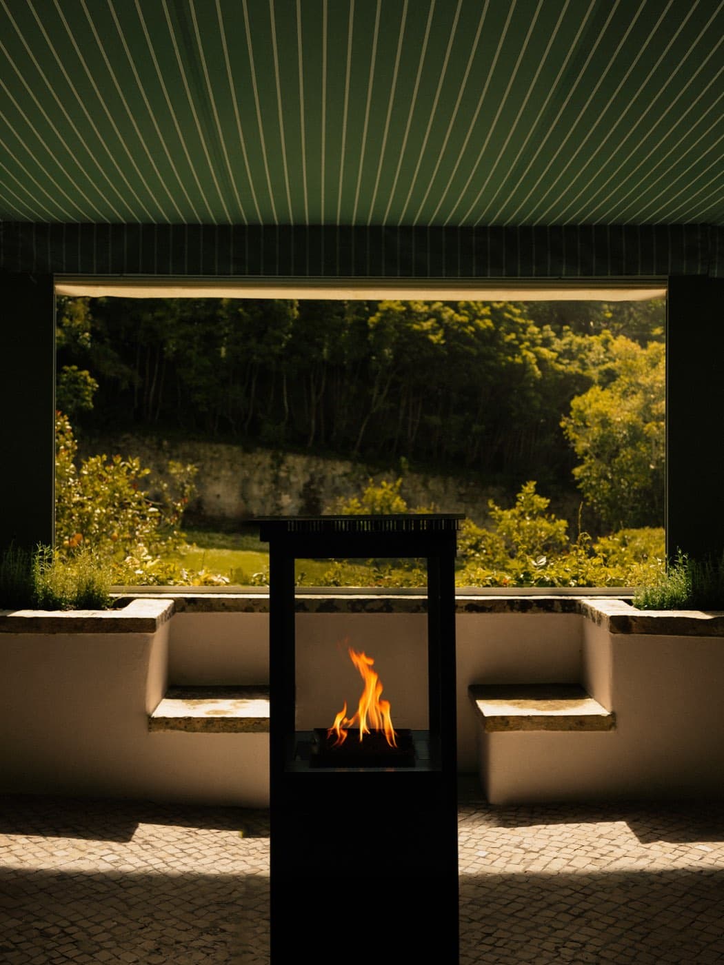 A fire burning in an open hearth under a green awning, the garden beyond.